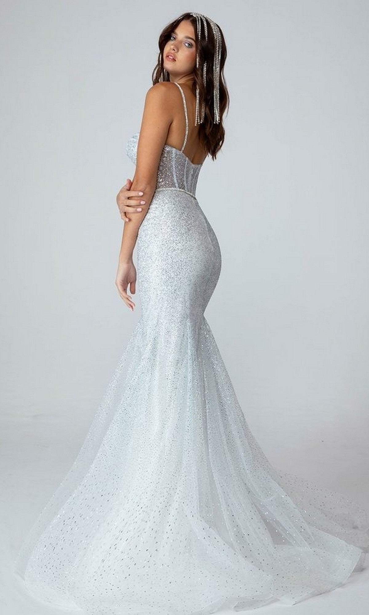 A woman models the Eureka 9911 long prom dress—a sparkly, fitted mermaid-style silver gown with a corset bodice—standing slightly turned to the side against a plain light background.
